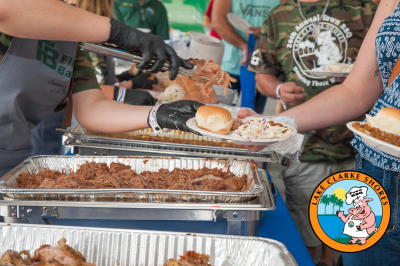 Volunteer handing out BBQ food to participants with BBQ pig logo on bottom right side of picture