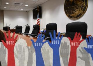 Graphic of raised hands over image of Lake Clarke Shores Council chamber